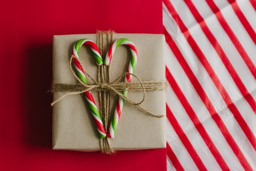 Gift box with candies in the form of a cane. Candy tricolor. Red background. Christmas lollipops.