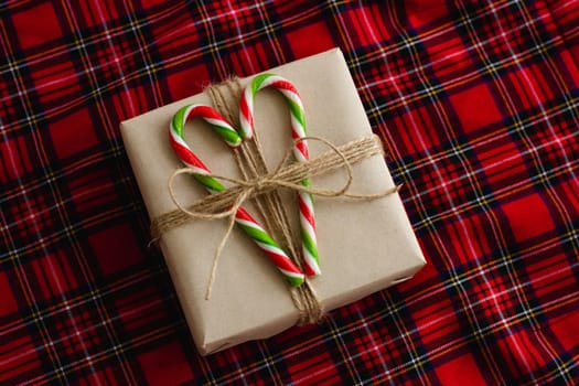 Gift on a checkered background. Gift box with candies in the form of a cane. Candy tricolor. Christmas lollipops. Checkered fabric in the background.