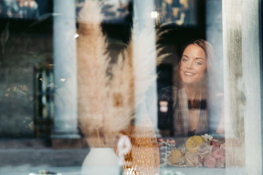 Portrait of a young European girl with long hair in a cafe sitting near the window, a tall girl in a jacket with long hair in the reflection of the window in a cafe.