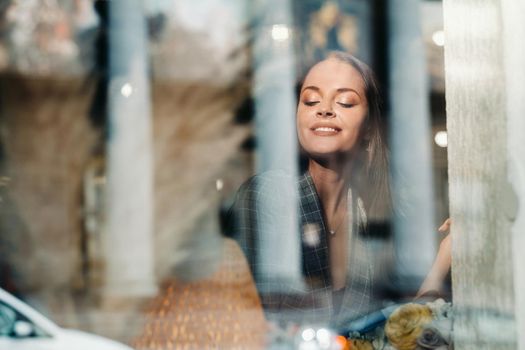 Portrait of a young European girl with long hair in a cafe sitting near the window, a tall girl in a jacket with long hair in the reflection of the window in a cafe.