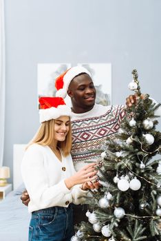 The family decorates the Christmas tree. A young man with a lovely wife helps her decorate the Christmas tree