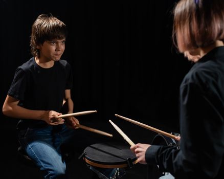 Young caucasian woman teaches a boy to play the drums in the studio on a black background. Music school student.