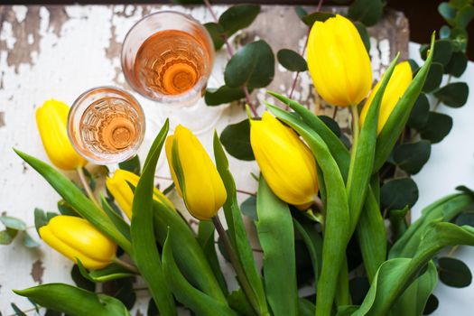 yellow tulips on a white table with a glass of rose wine, close-up