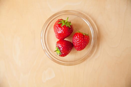 strawberries in a glass bowl on a wooden background