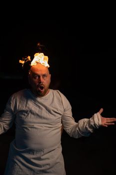 Bald man in a straitjacket with a burning head on a dark background