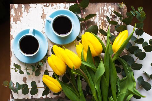 two blue cup of coffee with yellow tulips on an old table, close-up