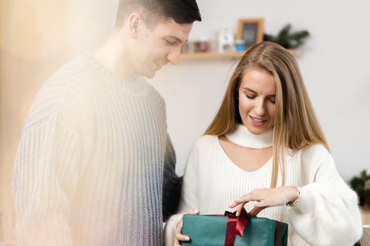 Sweet young couple opening Christmas gifts in the living room at home