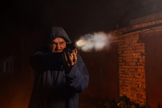 Caucasian man in a hood shoots a pistol