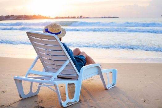 Beautiful girl in a hat sits on a deckchair meeting the dawn.