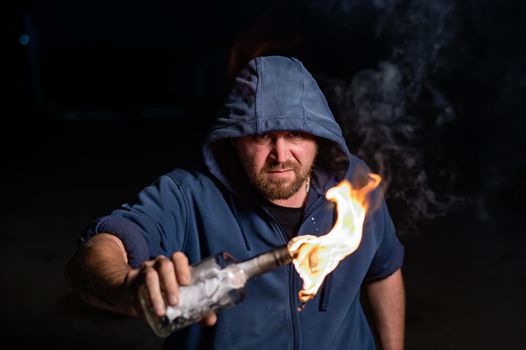 The man in the hood is holding a burning bottle. Molotov cocktail