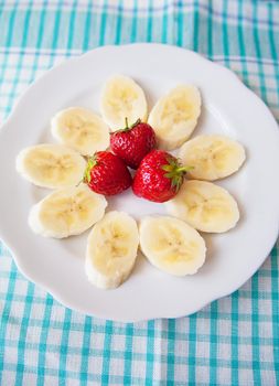 banana and strawberries on a white plate and a colorful napkin