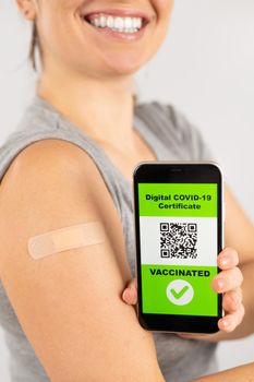 Woman with a plaster on her shoulder after vaccination and demonstrates the QR code on a smartphone