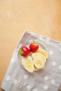 strawberry and banana on a glass plate on a wooden background