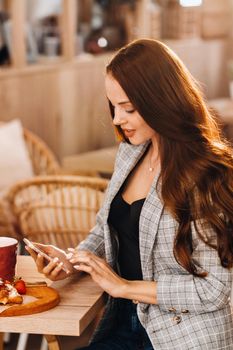 A girl is sitting at a table and texting on her smartphone in a cafe.A girl is sitting in a coffee shop with a phone.Writes in the phone.