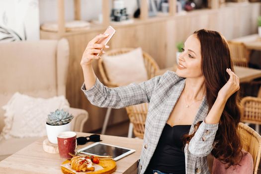 a business Girl is sitting in a cafe and taking a selfie,a Girl in a coffee shop is smiling and taking a selfie on a smartphone.