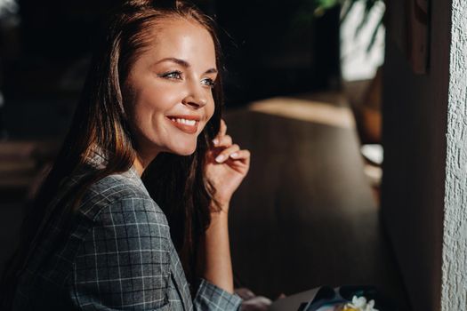 Portrait of a young European girl with long hair in a cafe with a bouquet standing near the window, a tall girl in a jacket with long hair in a cafe waiting.