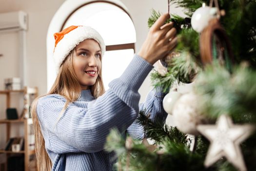 Young blonde woman on blue sweater decorating Christmas tree, close up