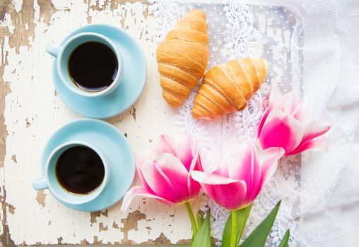 nice cup of coffee, croissants and pink tulips on old white table.