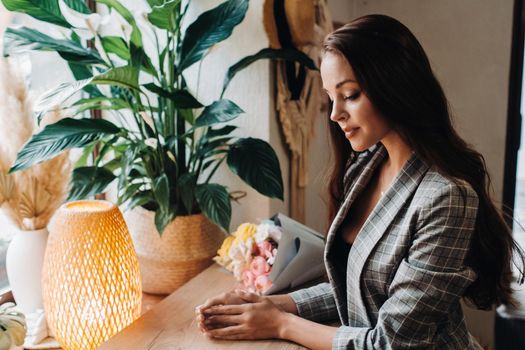 Portrait of a young European girl with long hair in a cafe with a bouquet standing near the window, a tall girl in a jacket with long hair in a cafe waiting.