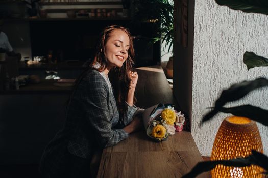 Portrait of a young European girl with long hair in a cafe with a bouquet standing near the window, a tall girl in a jacket with long hair in a cafe waiting.