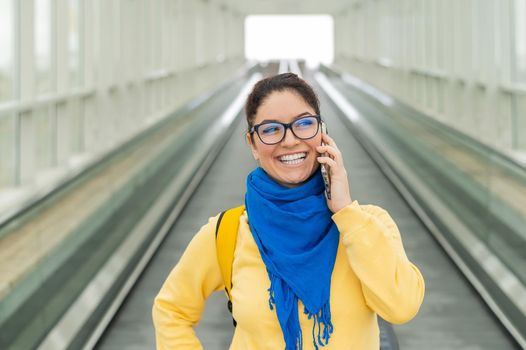 Happy woman stands on a travelator and talks on a cell phone.