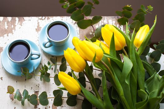 two blue cup of coffee with yellow tulips on an old table