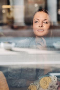 Portrait of a young European girl with long hair in a cafe sitting near the window, a tall girl in a jacket with long hair in the reflection of the window in a cafe.