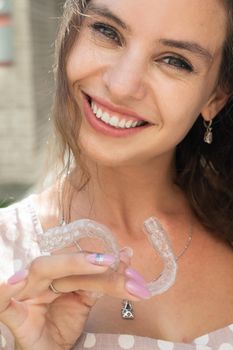 Beautiful caucasian woman holding transparent mouth guards for bite correction. Girl with silicone braces outdoors