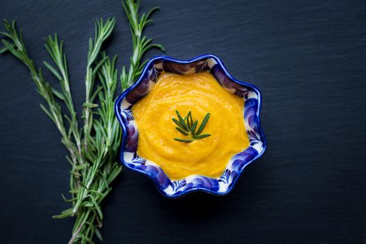 delicious pumpkin cream soup and black background with rosemary