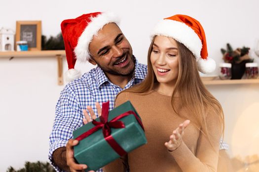 Romantic multiethnic couple in Christmas hats exchanging gifts, close up portrait