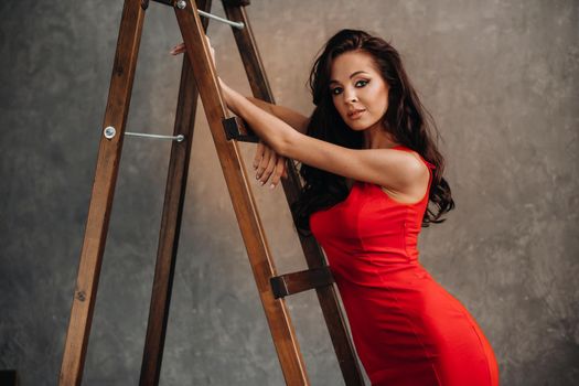 a brunette with long hair in a red dress poses in the studio near the stairs.