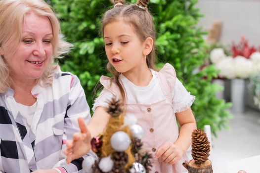 Elderly caucasian woman making pine cones decoration for christmas with two granddaughters.