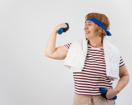 An elderly woman with a blue bandage on her head trains with dumbbells on a white background.