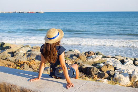 Beautiful girl in a hat sits near the sea on stones.