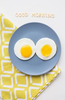 two eggs on a plate and a yellow napkin, inscription Good Morning