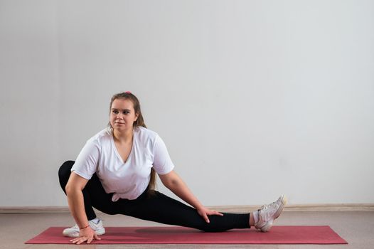 Young fat woman doing flexibility exercises on a white background.