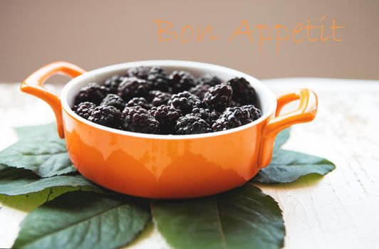 A full plate of blackberry stands on an old wooden background, the inscription bon appetit.