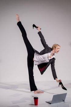 Barefoot ballerina dressed in a business suit poses for a laptop and drinks coffee. Flexible woman works at the computer.