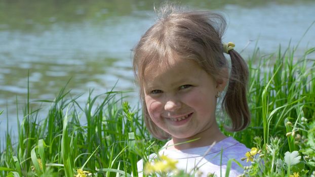 Portrait of a smiling little girl. Baby girl sitting in tall grass. Tiny kid have fun, enjoy nature outdoors.