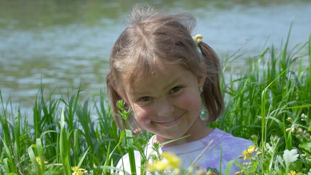 Portrait of a smiling little girl. Baby girl sitting in tall grass. Tiny kid have fun, enjoy nature outdoors.