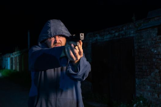 Caucasian man in a hood shoots a pistol