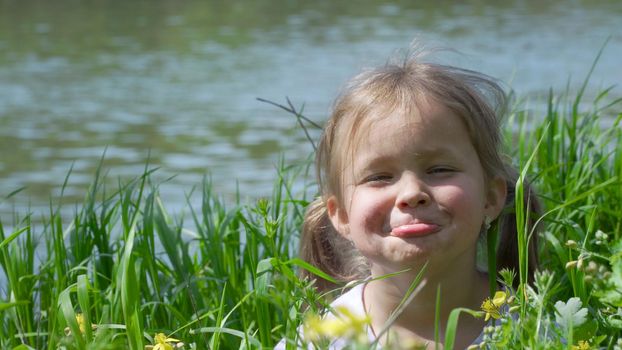 Portrait of a smiling little girl. Baby girl sitting in tall grass. Tiny kid have fun, enjoy nature outdoors.