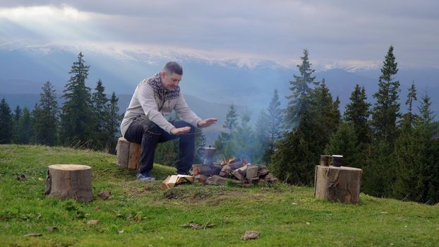 A man prepares morning coffee near a campfire in the mountains. Travel concept