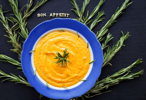 pumpkin soup with rosemary branches on a black background with a blue napkin