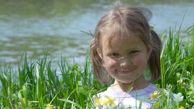 Portrait of a smiling little girl. Baby girl sitting in tall grass. Tiny kid have fun, enjoy nature outdoors.