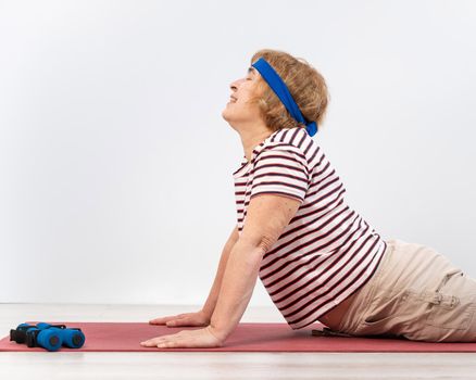 Elderly woman doing exercises in the studio on a white background. The old lady is doing fitness for health.