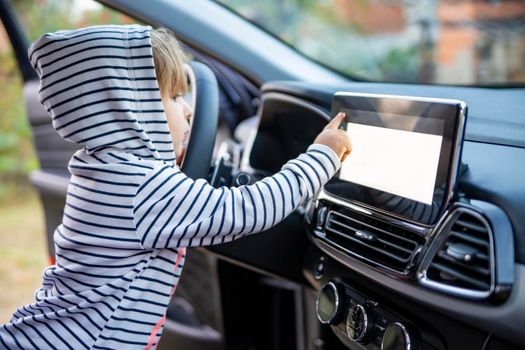 curious toddler girl holding, touching, and turning a car mnultiedia touch screen player button. empty white screen