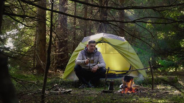 The man sits near the fire. Camping in a beautiful forest. The food in the cauldron is cooked over the fire. Travel concept