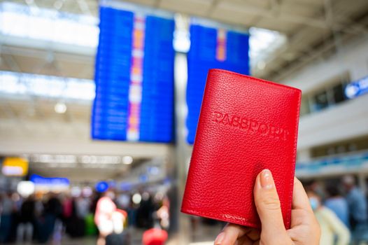 Woman holding a passport against the background of an airport information board