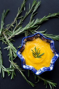 pumpkin soup on a black background with the sprigs of rosemary, close-up.